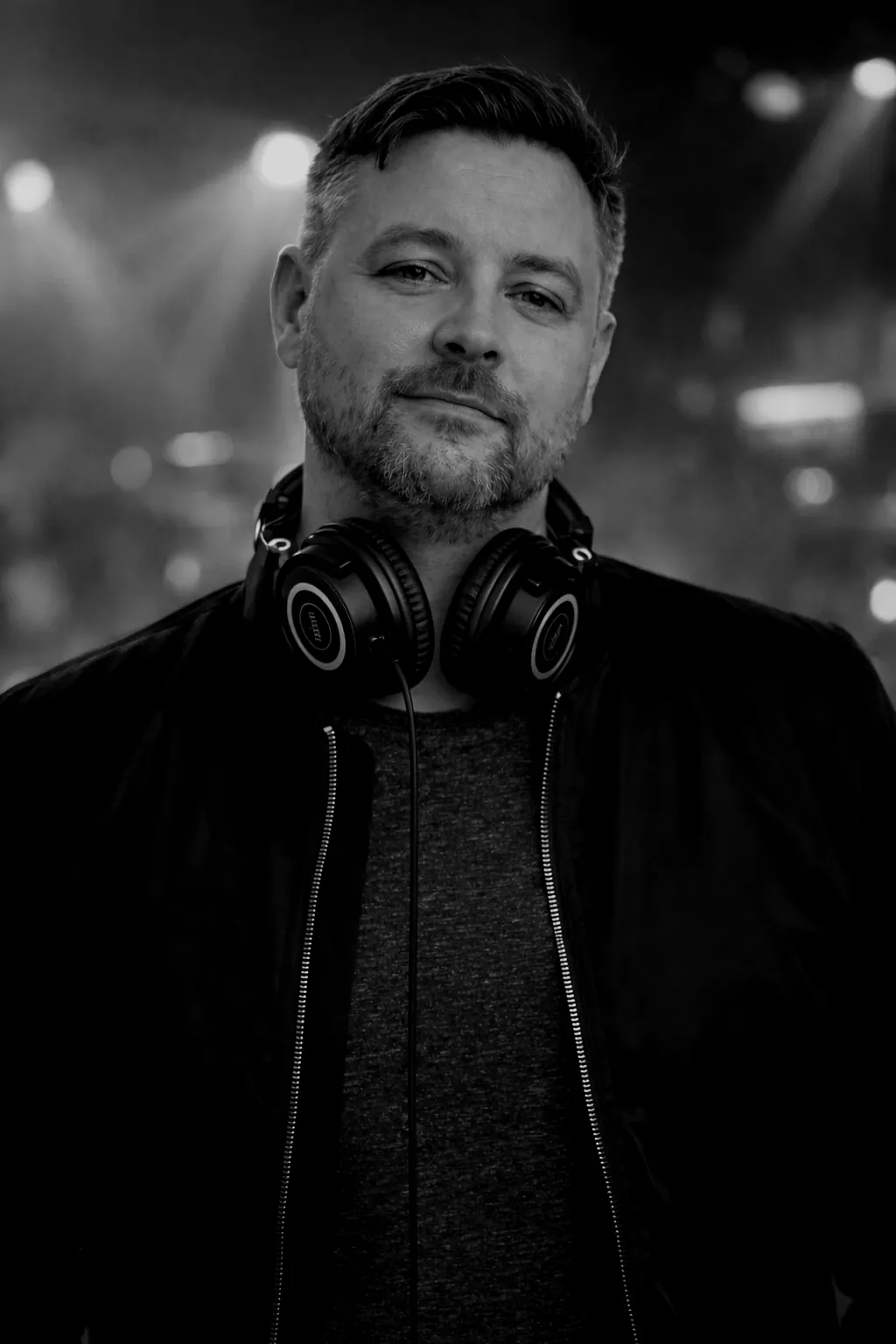 J5Dev in front of stage lights, headphones round the neck