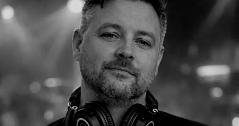 J5Dev in front of stage lights, headphones round the neck